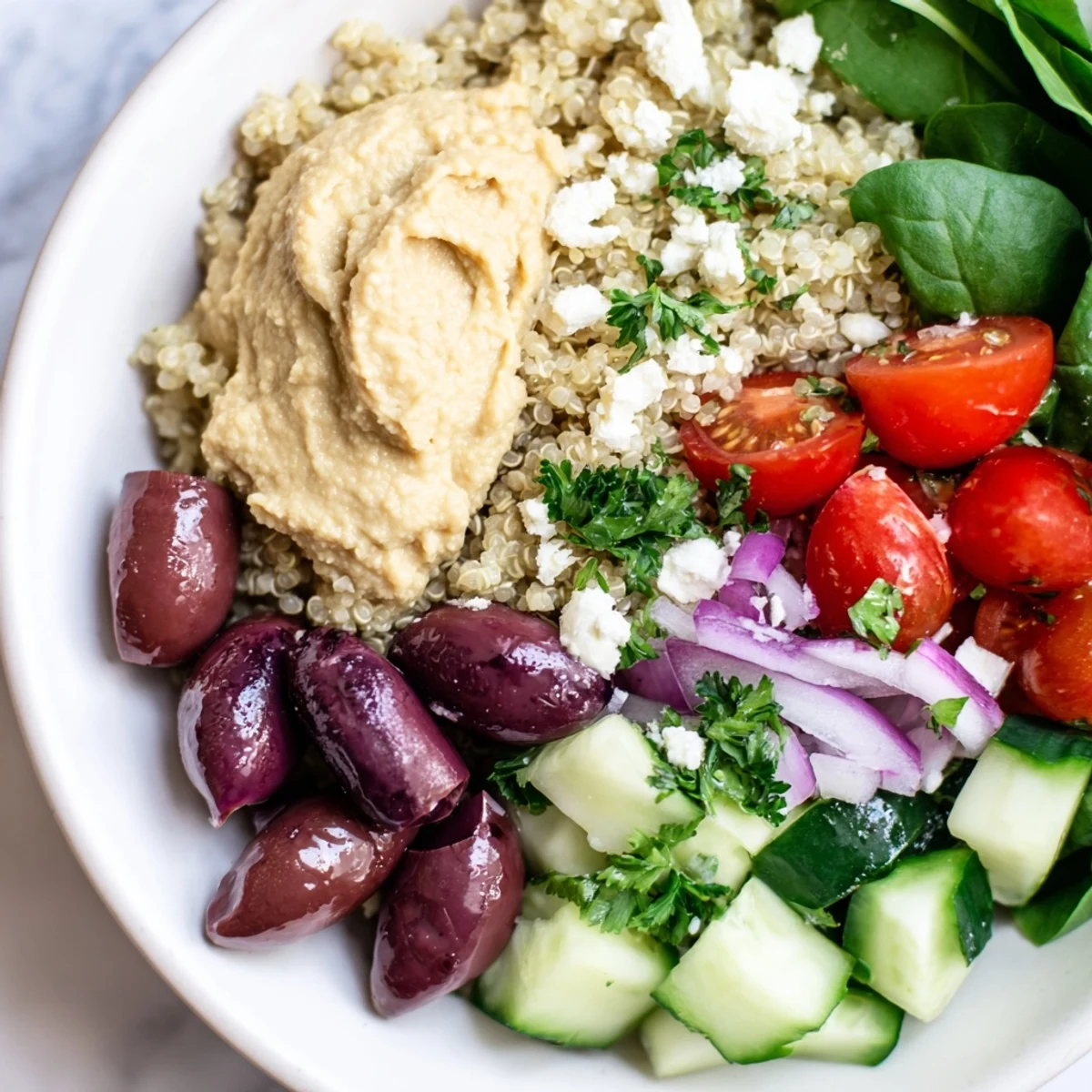 A close-up of a vibrant Mediterranean Quinoa Bowl topped with creamy hummus, briny Kalamata olives, and fresh chopped parsley.