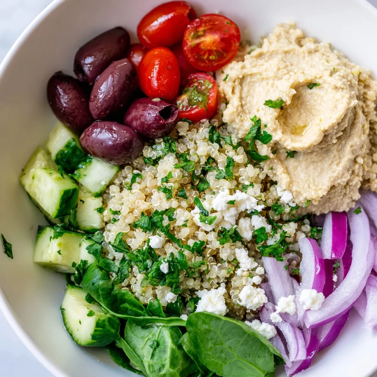 Overhead view of a Mediterranean Quinoa Bowl featuring a swirl of hummus, green spinach, and feta cheese crumbles.