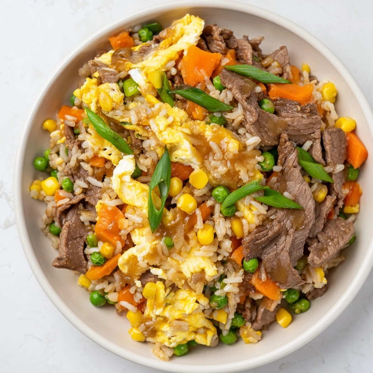 Heaping skillet of Beef Fried Rice with Mixed Vegetables and Egg, garnished with green onions and sesame seeds, ready to enjoy.