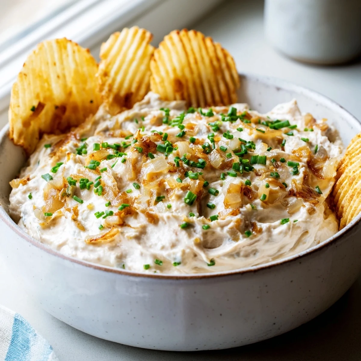 A close-up of Game Day Onion Dip garnished with fresh chives, a dollop on a sturdy chip for the perfect savory game day bite.