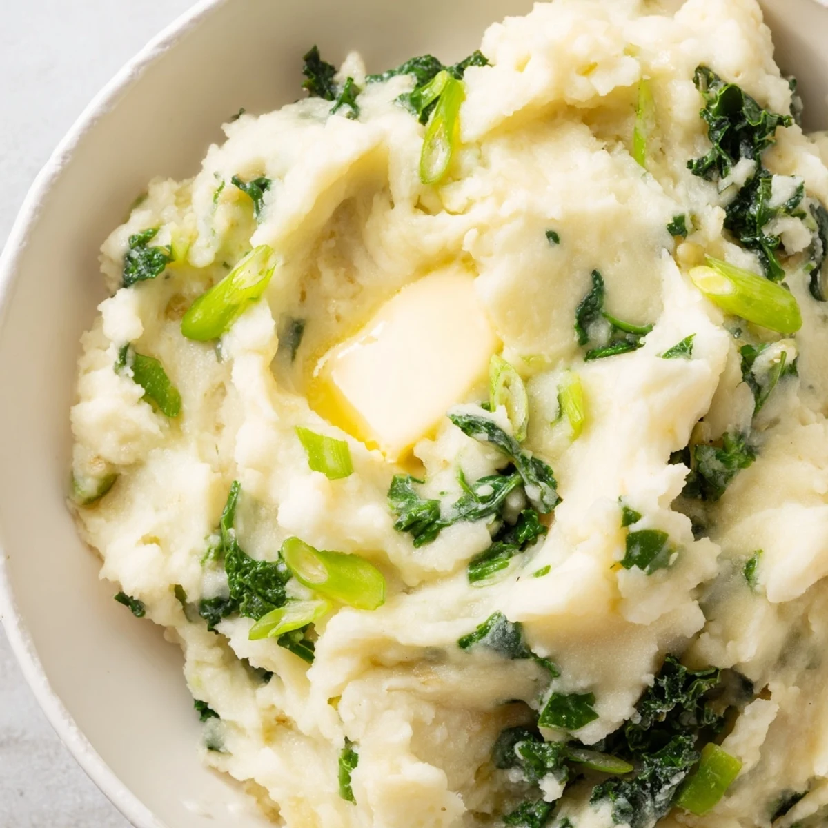 A rustic bowl of homemade Irish Colcannon, blending buttery mashed potatoes with hearty kale and a garnish of sliced scallions.
