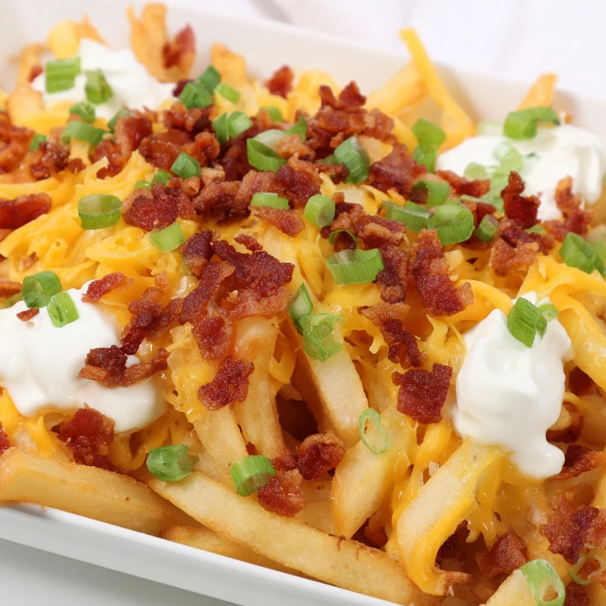 Sizzling, oven-baked fries piled high with cheddar, bacon, and fresh green onions, served hot for a game day feast.