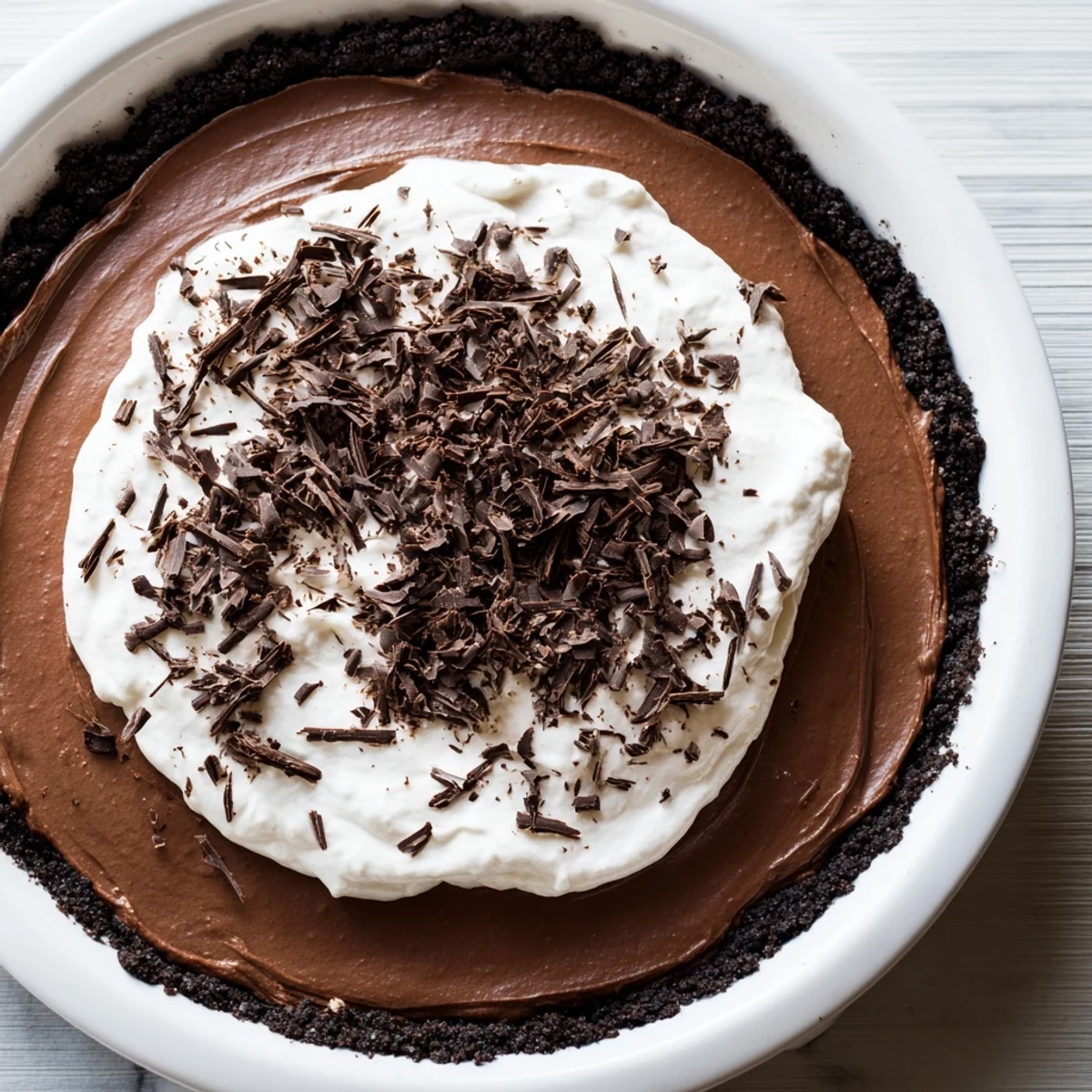 A close-up of a slice of Romantic Chocolate Silk Pie on a dessert plate, showing the rich chocolate filling and whipped cream topping.