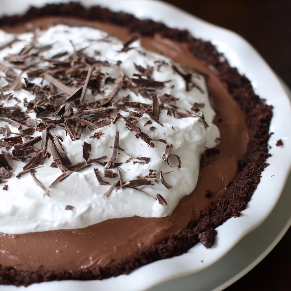 Fresh raspberries and chocolate shavings garnish a whole Romantic Chocolate Silk Pie, resting on a rustic wooden table.