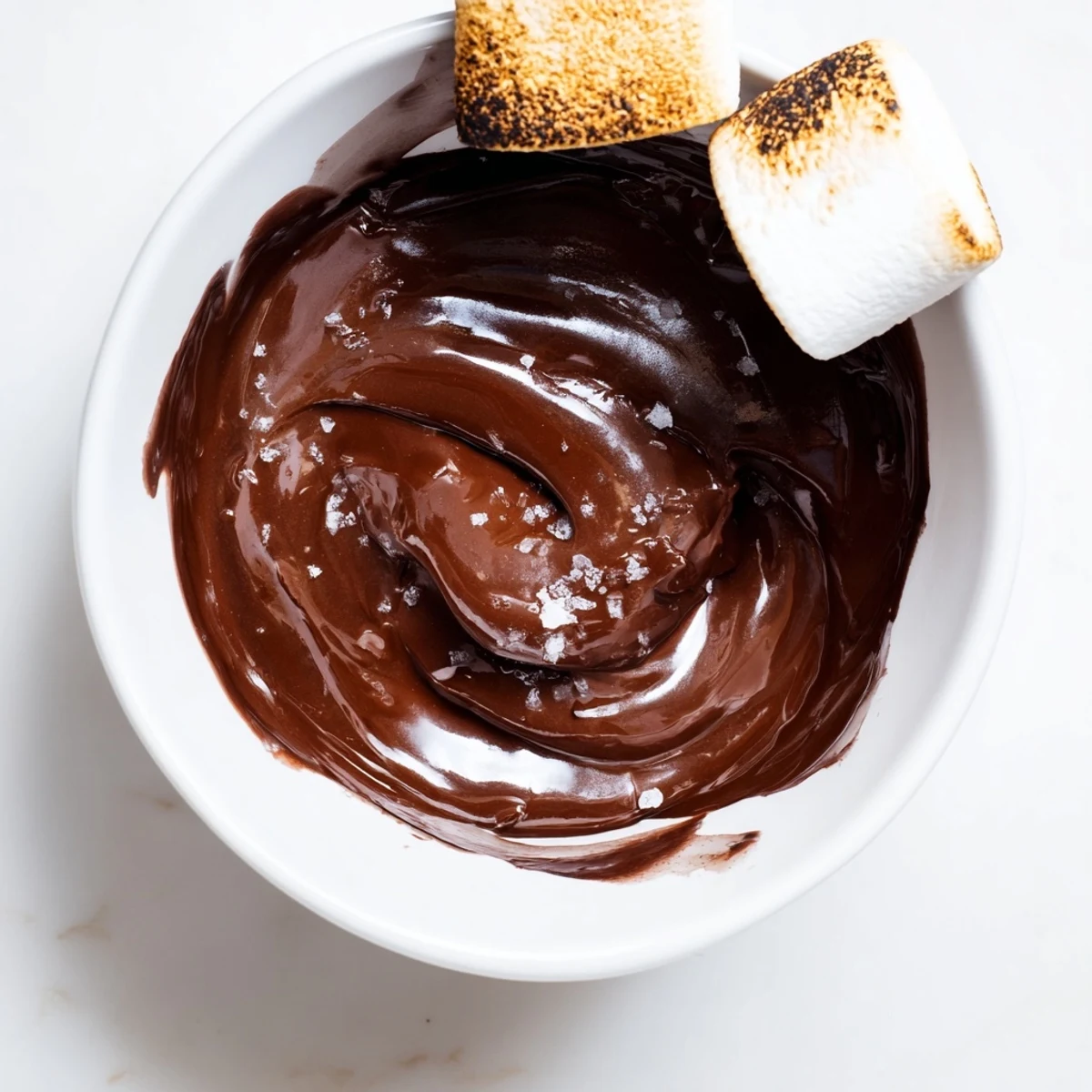 Up close on a rustic wooden table, Romantic Chocolate Fondue with Marshmallows shows rich, dark chocolate swirled with cream, a glossy pool perfect for dipping. A hand holds a skewer with a ripe banana slice and strawberry, half-dipped in the warm chocolate. A pinch of sea salt and vanilla are hinted in the sensory richness.