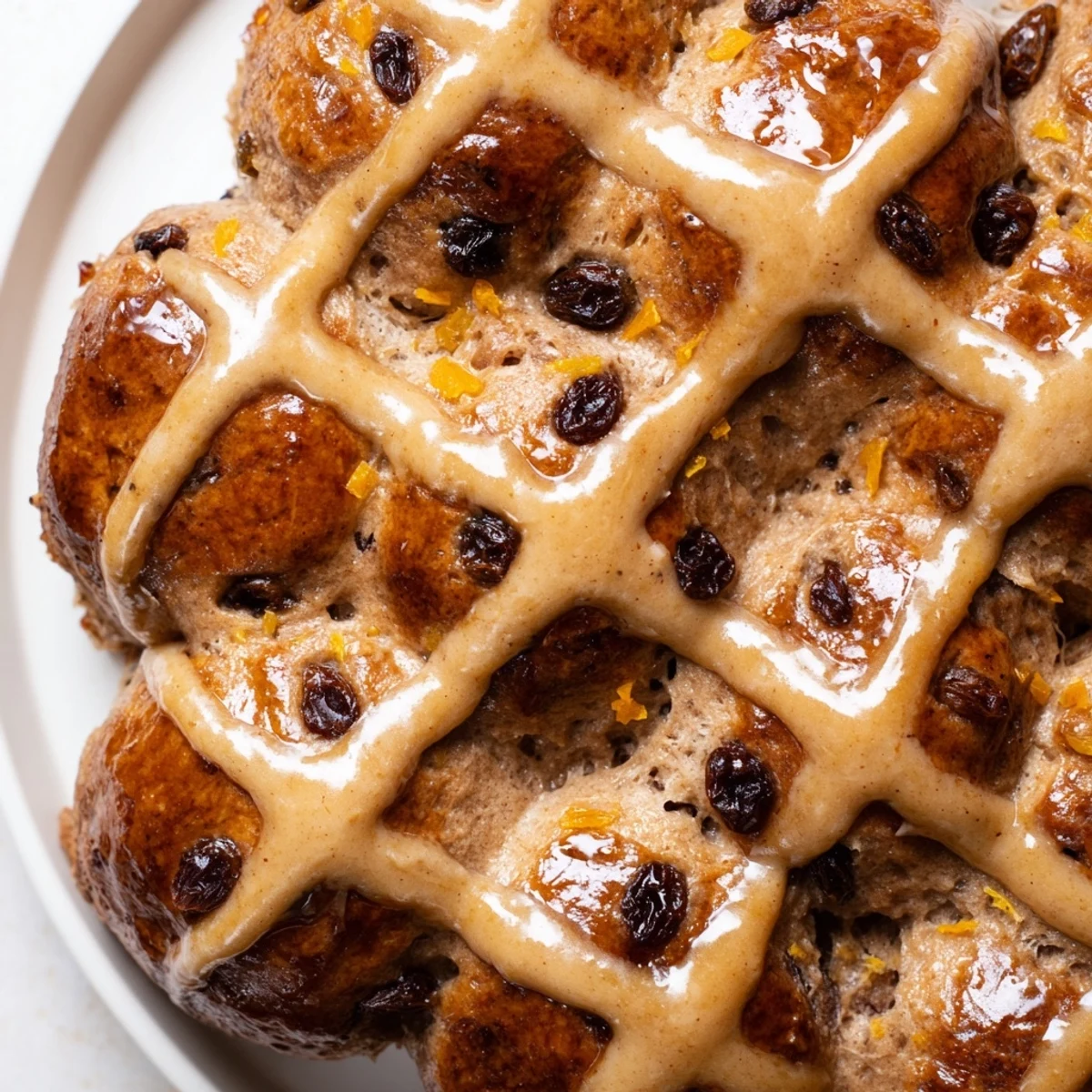 Savory Hot Cross Buns with Raisins and Orange Glaze fresh from the oven on a white plate with a linen napkin.
