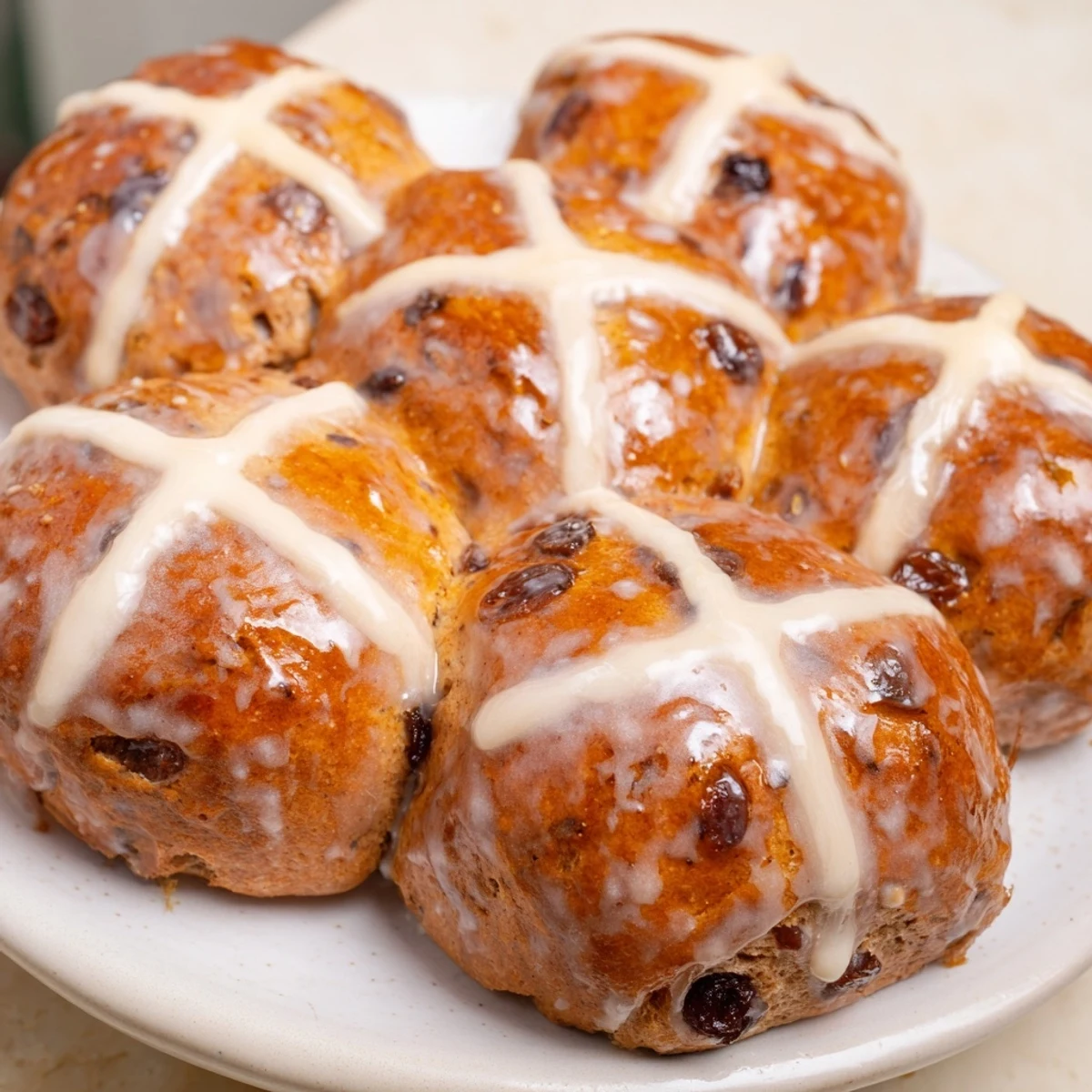 Golden-brown Hot Cross Buns with Currants and Spices rest on a cooling rack after baking.