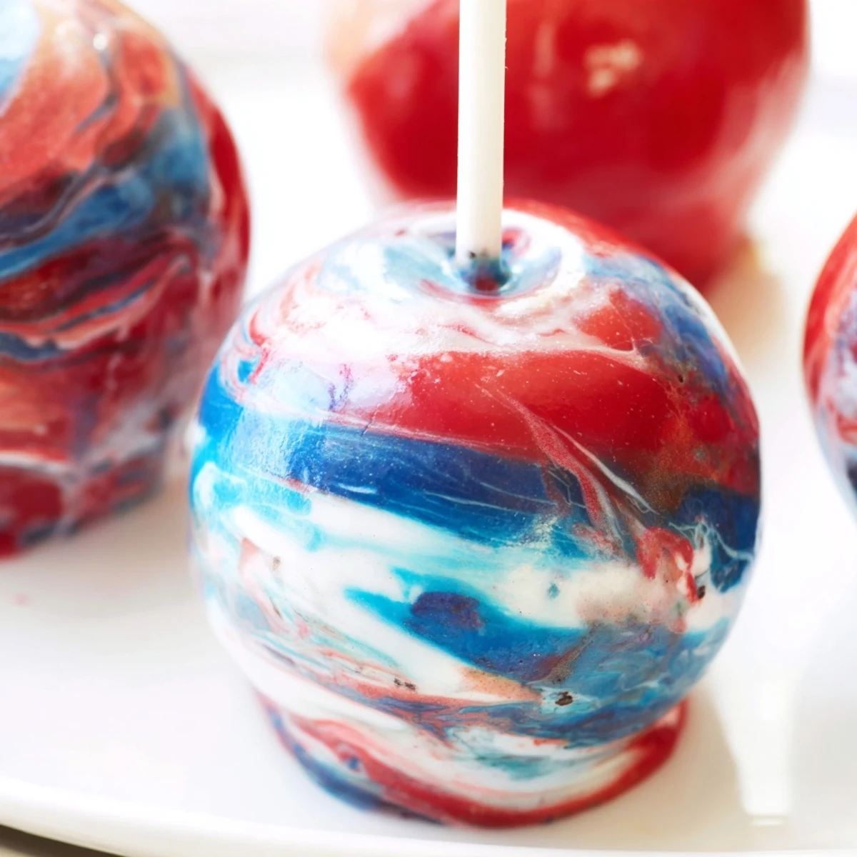 A close-up of marbled effect candy apples with a glossy, swirled red, blue, and white candy shell on a dessert table.