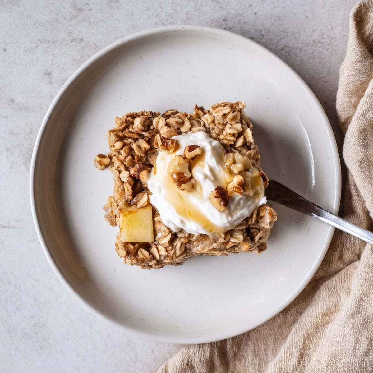 A close-up of Baked Apple Oatmeal with Greek Yogurt, featuring a golden-brown square topped with creamy yogurt and chopped walnuts.  