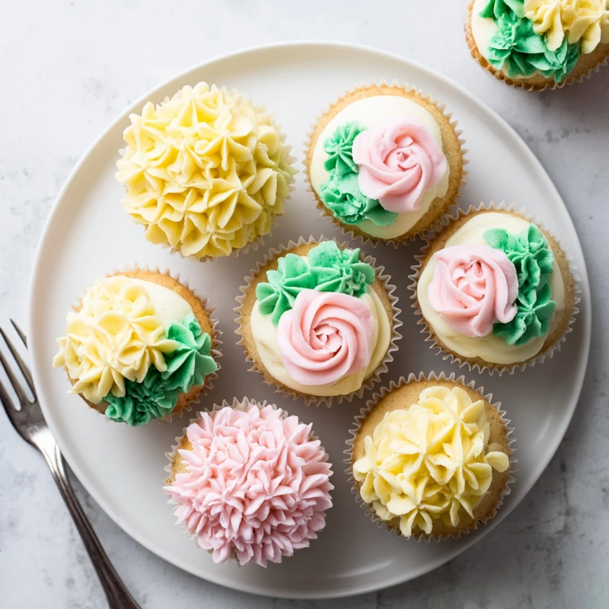 Golden pink and yellow frosted Baby In Bloom Cupcakes sit on a white pedestal, topped with delicate edible pansies and pastel nonpareils, ready for a spring celebration.