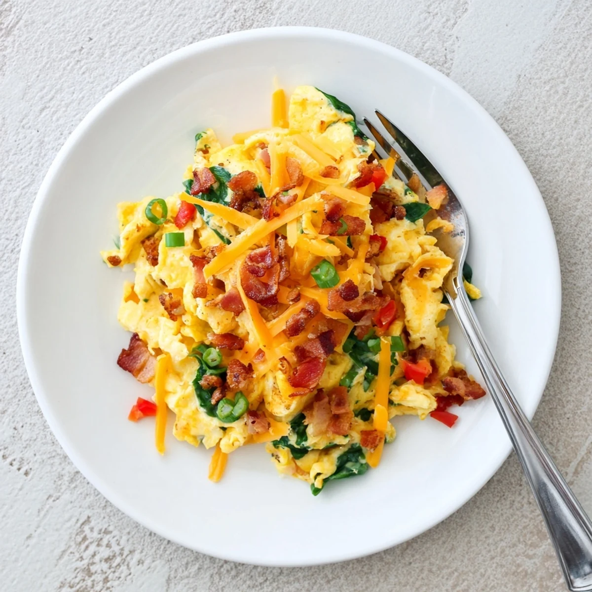 Golden Loaded Scrambled Eggs with crispy bacon and melted cheddar cheese in a skillet for breakfast.  