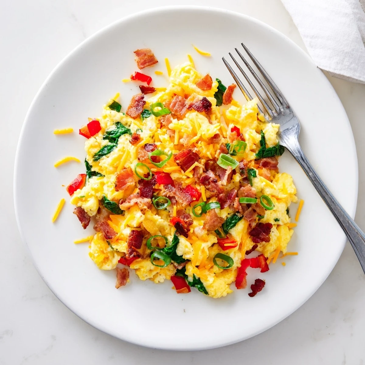 Plated Loaded Scrambled Eggs topped with green onions and sautéed red peppers beside toast.  
