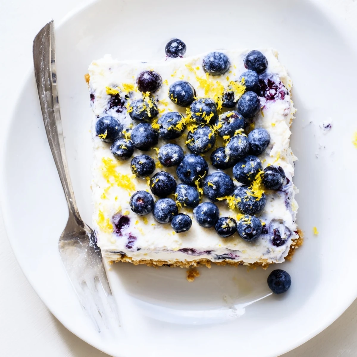 Creamy no bake lemon blueberry cake with whipped cream cheese filling and vibrant berry topping on white plate