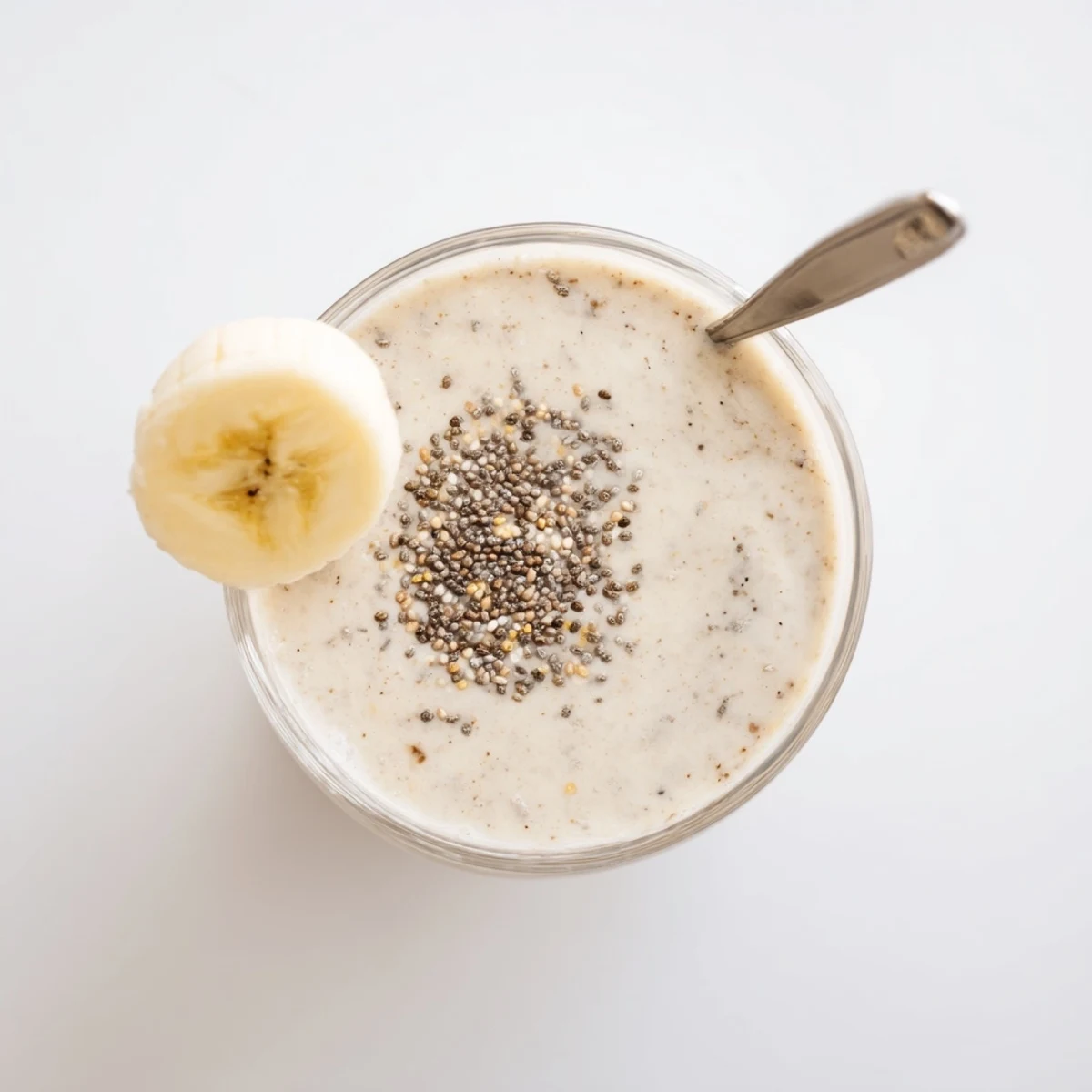 Fresh blended Greek yogurt banana smoothie with ice cubes and honey drizzle on wooden counter
