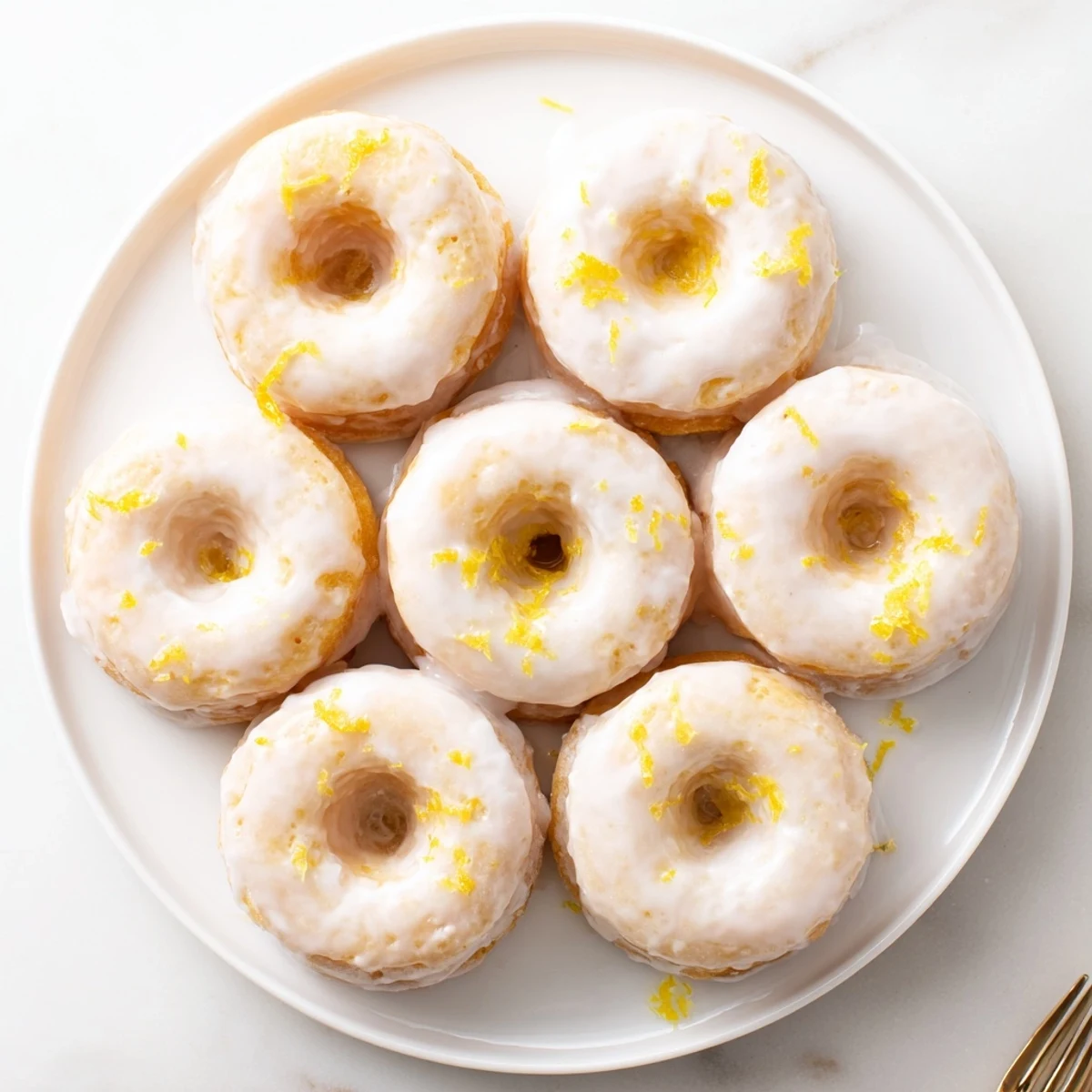 Glazed lemon mochi donuts displayed on a wooden board with fresh lemon zest garnish