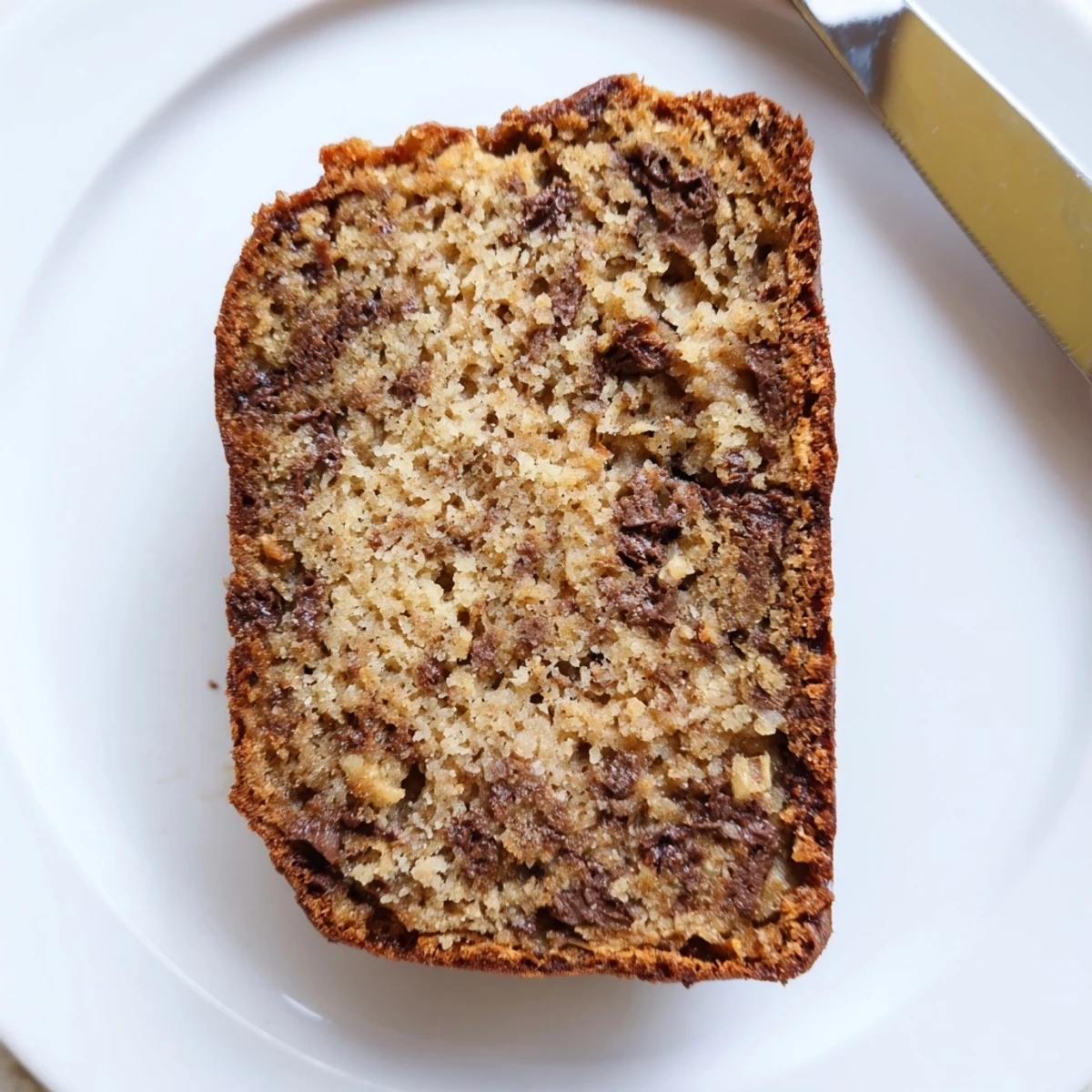 Thick slice of moist classic chocolate chip banana bread on a wooden cutting board