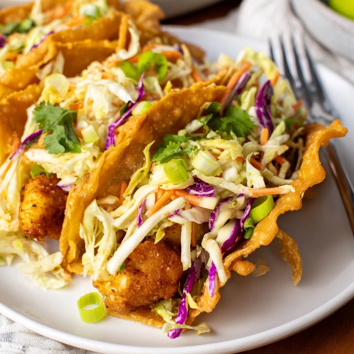 Golden crispy chicken wonton tacos piled high with colorful Asian slaw and drizzled with sweet chili sauce on a white plate