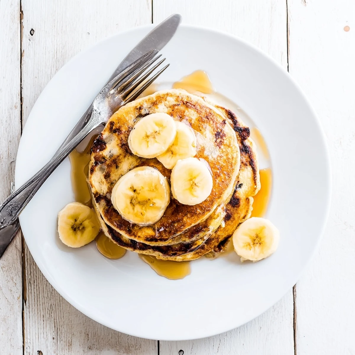 Golden stack of Greek yogurt banana pancakes drizzled with maple syrup and fresh berries on a white plate