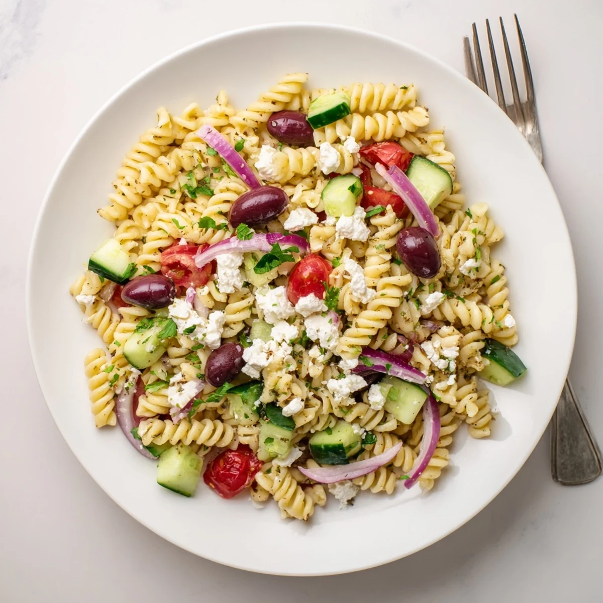 Greek pasta salad in a white bowl with crisp cucumbers, red onions, and feta