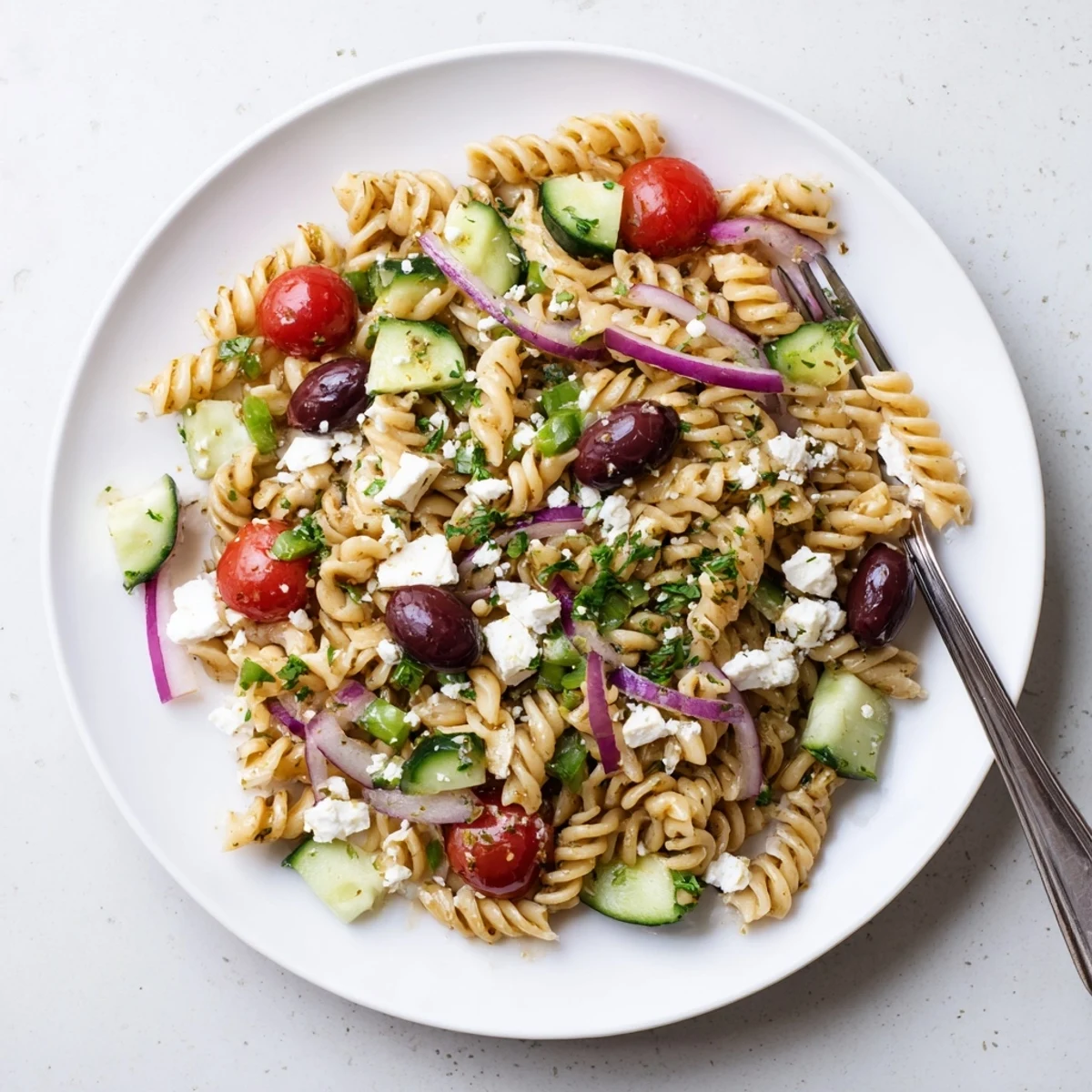 Colorful Greek pasta salad featuring cherry tomatoes, olives, and herbs on wooden table