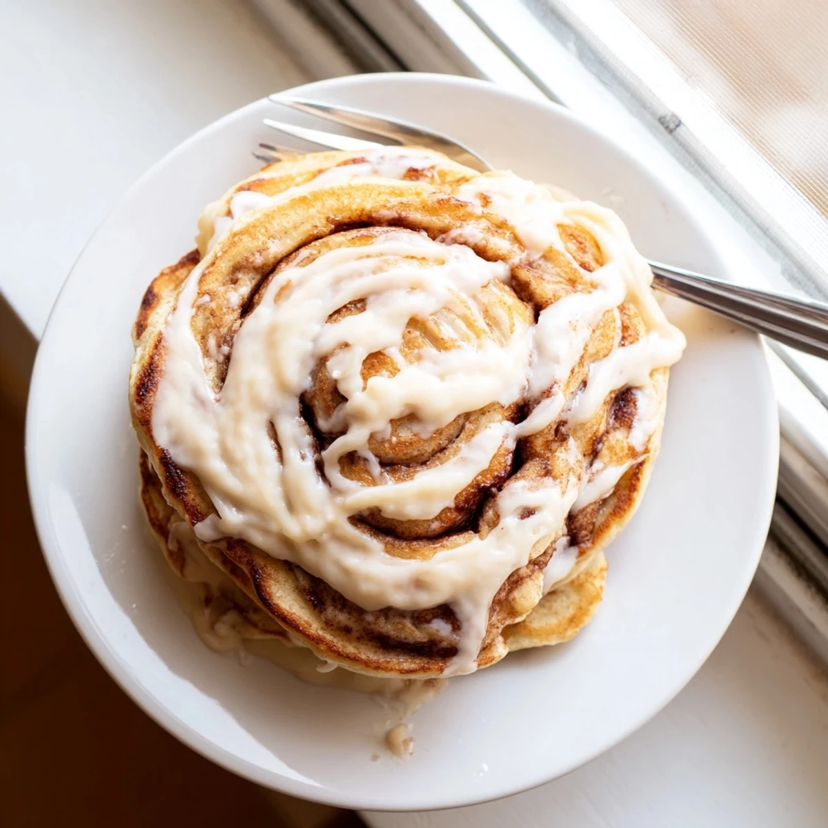 Stack of cinnamon roll pancakes topped with rich icing and chopped pecans.