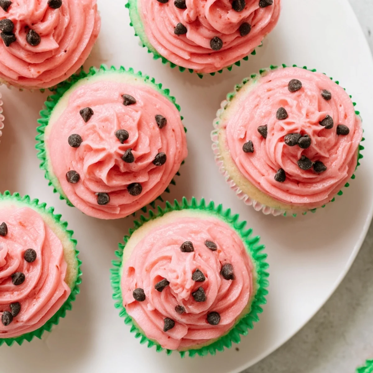 Moist vanilla watermelon cupcakes topped with fluffy pink frosting and mini chocolate chip seeds