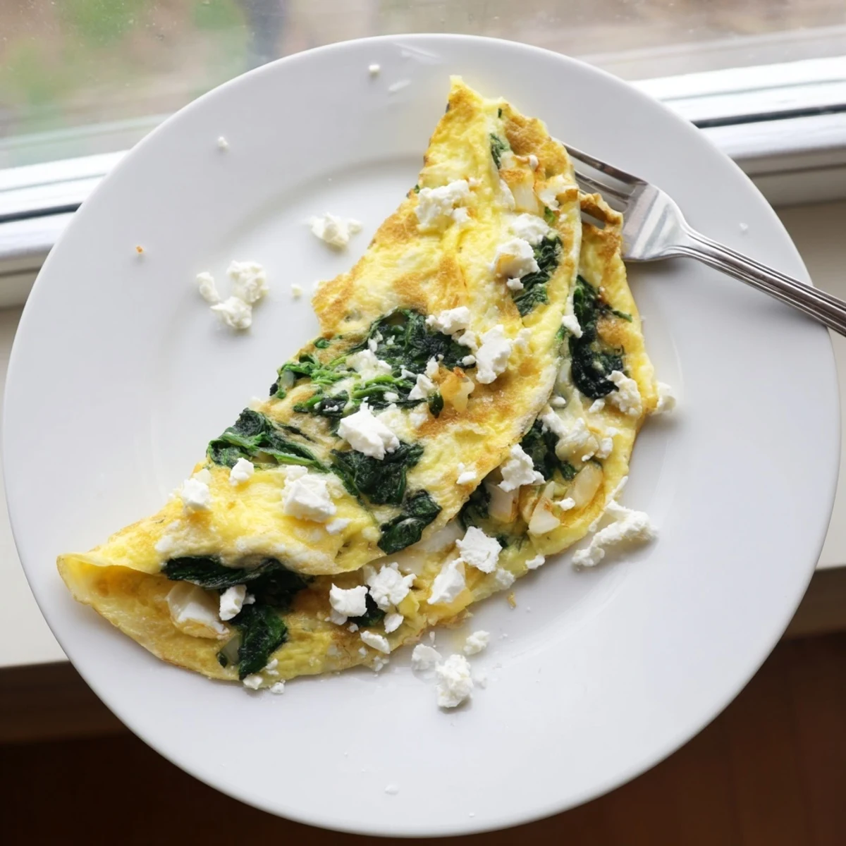 Golden folded spinach feta omelet garnished with extra crumbled cheese on white plate