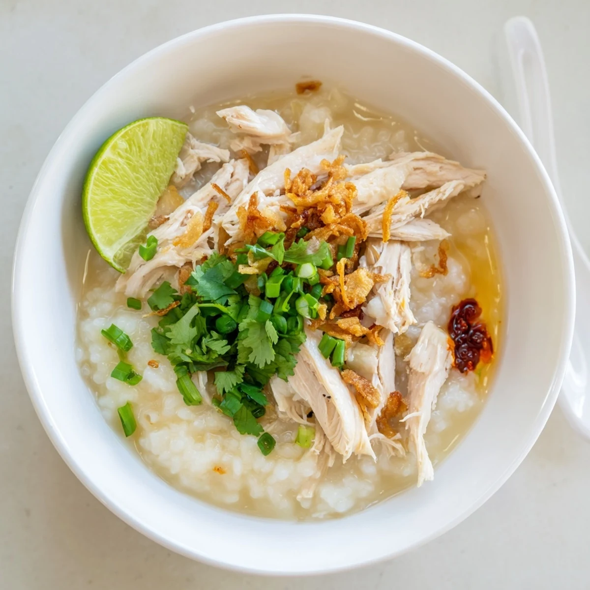 Creamy chao ga garnished with shredded chicken, scallions, and vibrant herbs in a deep ceramic bowl