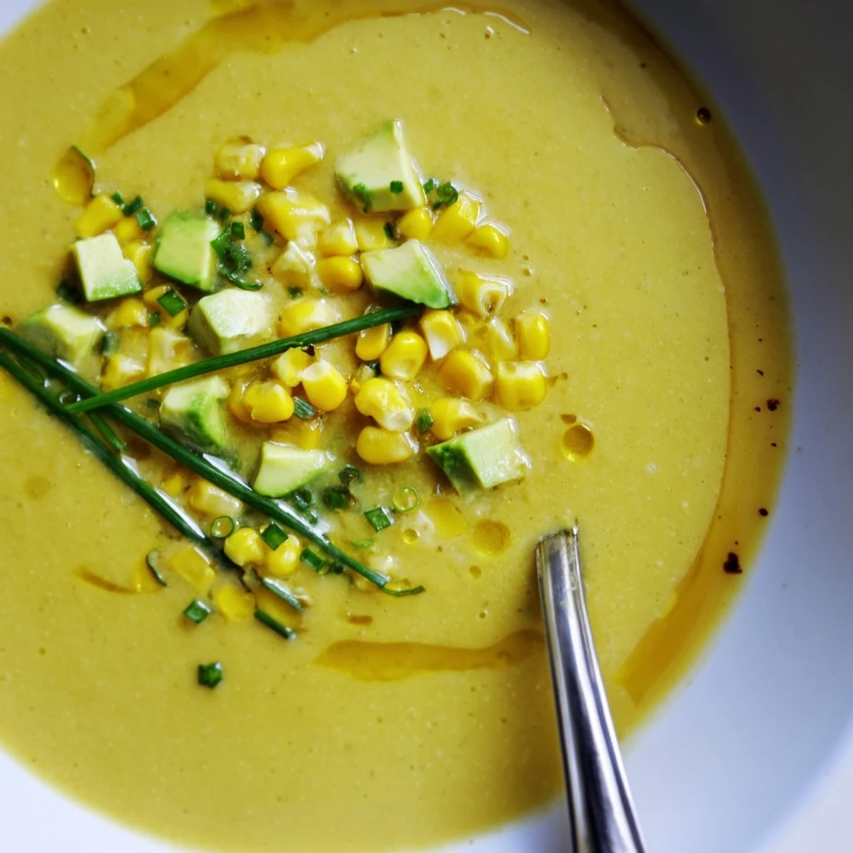 A bright yellow bowl of Summer Sweet Corn Gazpacho topped with avocado and fresh chives