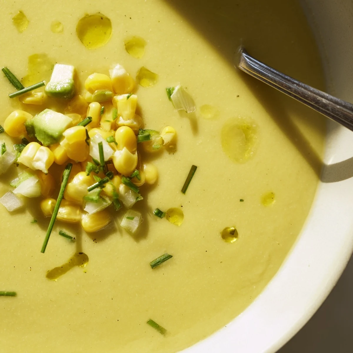 Chilled Summer Sweet Corn Gazpacho poured into a white bowl with a golden olive oil drizzle