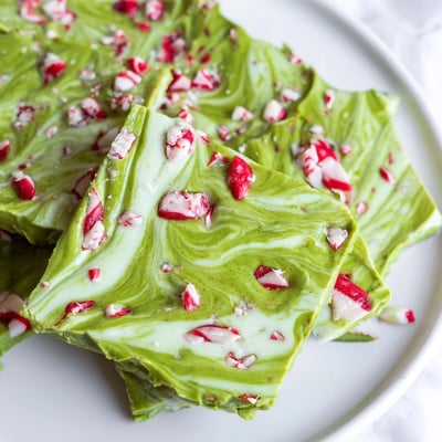 Pieces of homemade Matcha Peppermint Bark displayed on a plate beside a cup of steaming green tea.