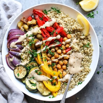 A warm vegan Mediterranean roasted vegetables bowl topped with zesty lemon tahini sauce and fresh parsley over quinoa.